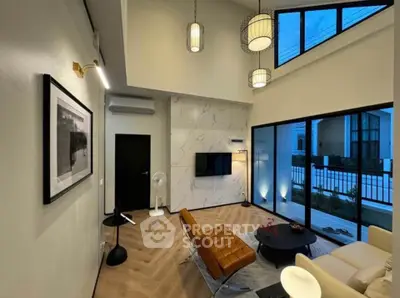 Modern living room with high ceiling and large windows, featuring stylish furniture and elegant lighting.