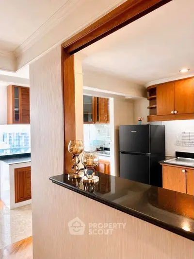 Spacious kitchen with modern black fridge and wooden cabinetry, featuring an open layout and elegant decor.