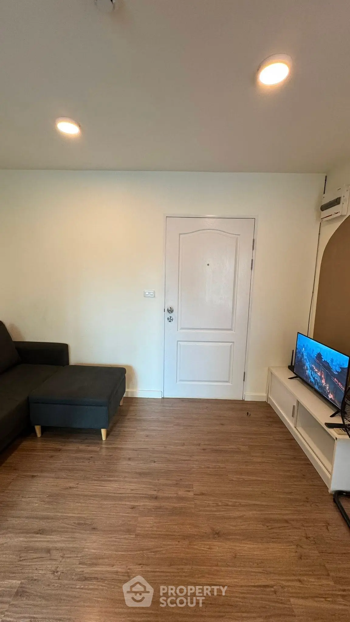 Modern living room with sleek wooden flooring and cozy sofa, featuring a flat-screen TV and minimalist decor.