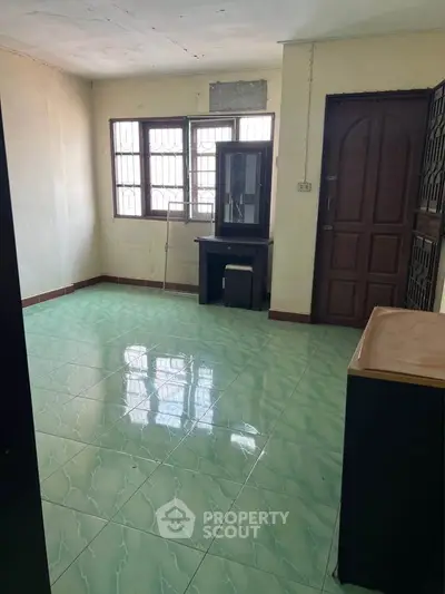Spacious unfurnished room with green tiled flooring and large windows.
