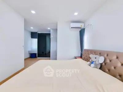 Spacious bedroom with modern decor and plush bedding, featuring an air conditioner and large window for natural light.