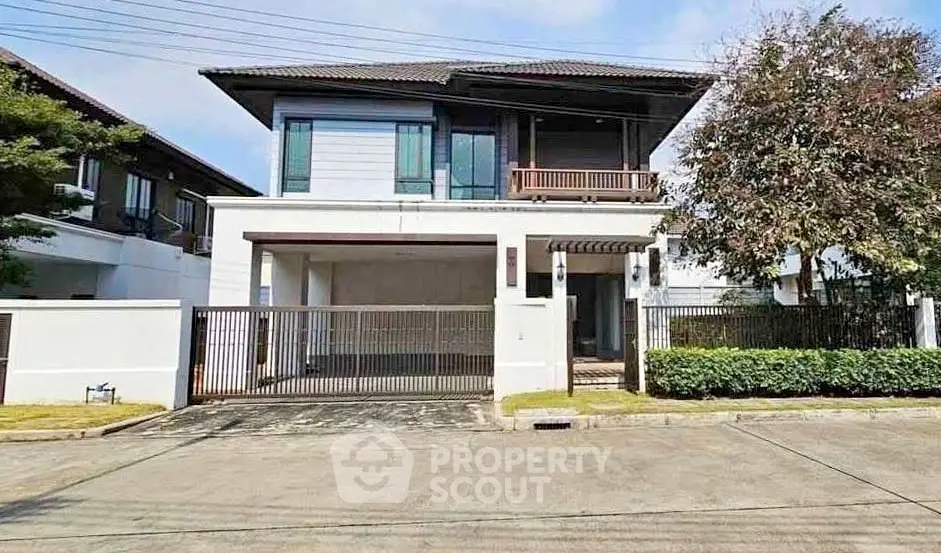 Modern two-story house with gated entrance and lush greenery in a serene neighborhood.