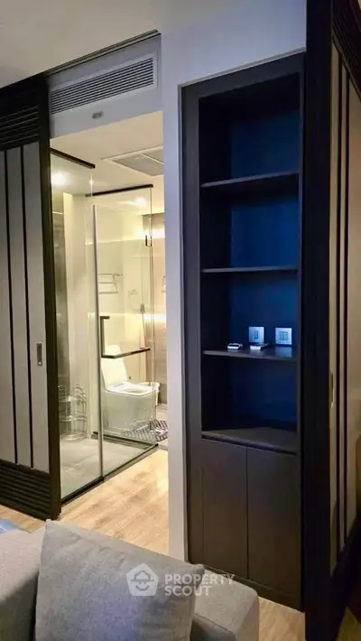 Modern apartment interior with glass-enclosed bathroom and sleek shelving unit.