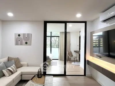 Modern living room with sliding glass doors leading to a cozy bedroom, featuring stylish decor and natural light.