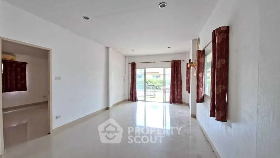 Spacious living room with large windows and polished floors, offering ample natural light and a modern feel.