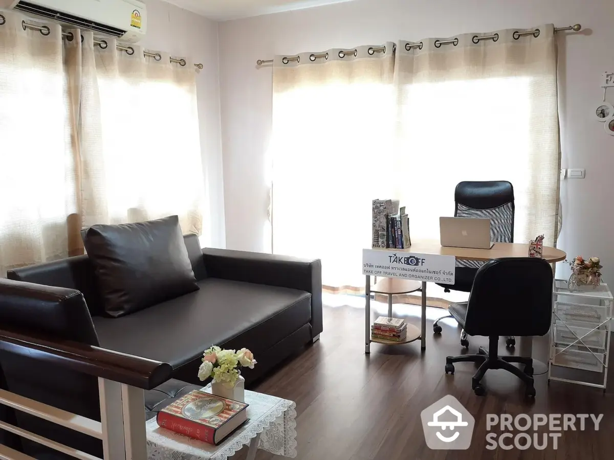 Inviting living space with ample natural light, featuring a sleek dark sofa, modern office area, and warm wooden accents.