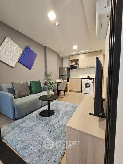 Modern living room with cozy sofa, stylish decor, and compact kitchen featuring washing machine.