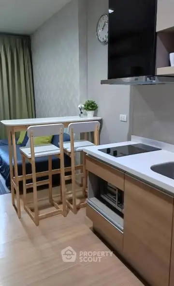 Modern kitchen with sleek countertops and wooden bar stools in a cozy apartment setting.