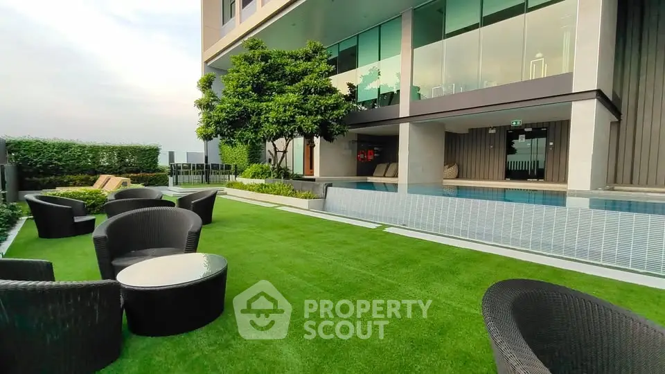 Luxurious modern building exterior with lush garden and poolside seating area.
