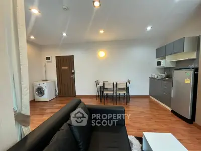 Modern open-layout living room with kitchen and dining area, featuring sleek furniture and wooden flooring.