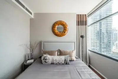 Modern bedroom with large windows and city view, featuring stylish decor and neutral tones.