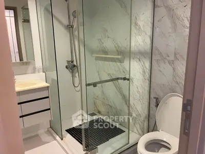 Modern bathroom with glass shower and marble walls in a stylish apartment.
