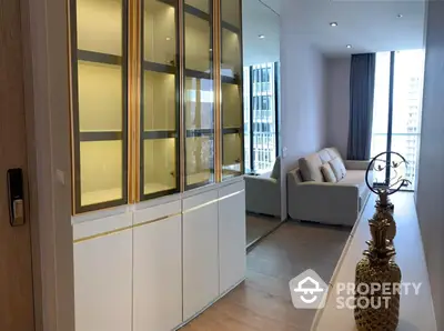 Elegant modern living room with sleek white storage cabinets, gold accents, and a cozy seating area, bathed in natural light from large windows.