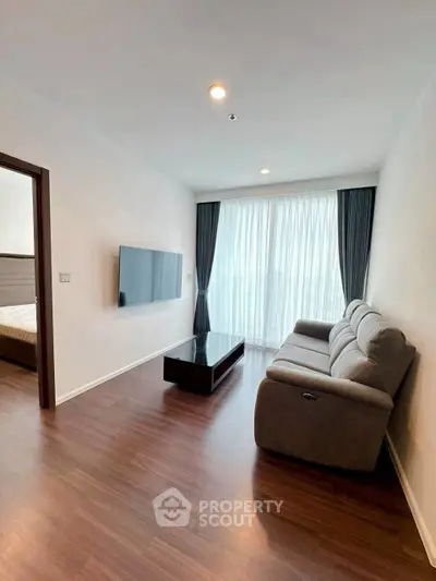 Modern living room with sleek sofa and wall-mounted TV, featuring elegant wooden flooring and large window.