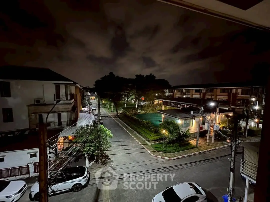 Nighttime view of residential street with parked cars and illuminated homes.