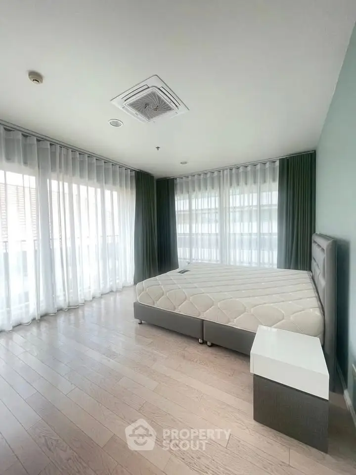 Spacious bedroom with large windows and modern furnishings in a bright apartment.