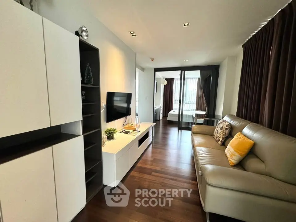 Modern living room with sleek furniture and open view to bedroom, featuring hardwood floors and stylish decor.