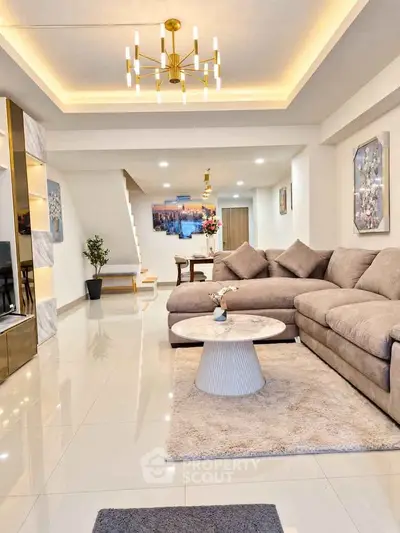 Luxurious modern living room with elegant chandelier and plush sectional sofa in open layout.