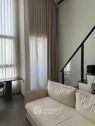 Modern living room with high ceilings and staircase, featuring a cozy sofa and natural light.
