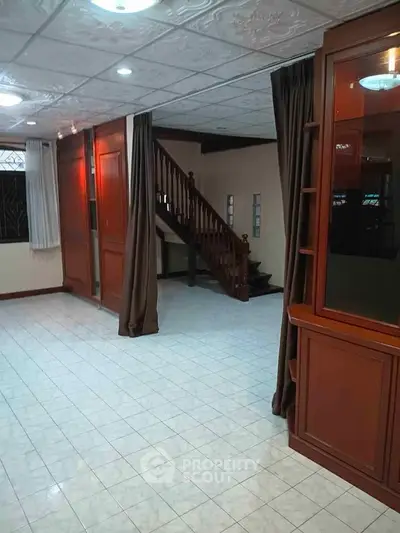 Spacious living room with elegant wooden staircase and tiled flooring, perfect for family gatherings.