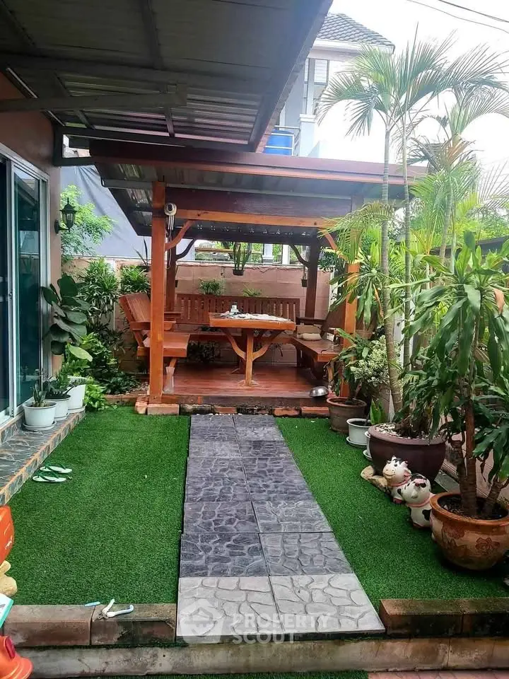 Charming garden patio with lush greenery and cozy wooden seating area, perfect for outdoor relaxation.