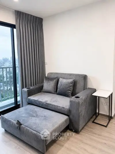 Modern living room with stylish gray sofa and city view from balcony.