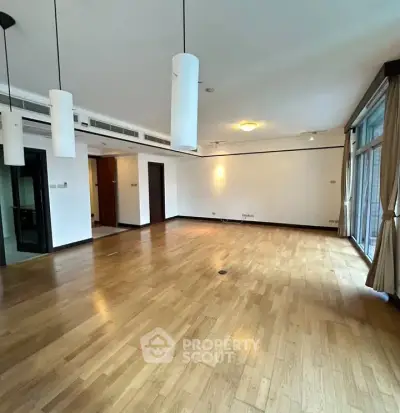 Spacious empty living room with wooden flooring and large windows in modern apartment.
