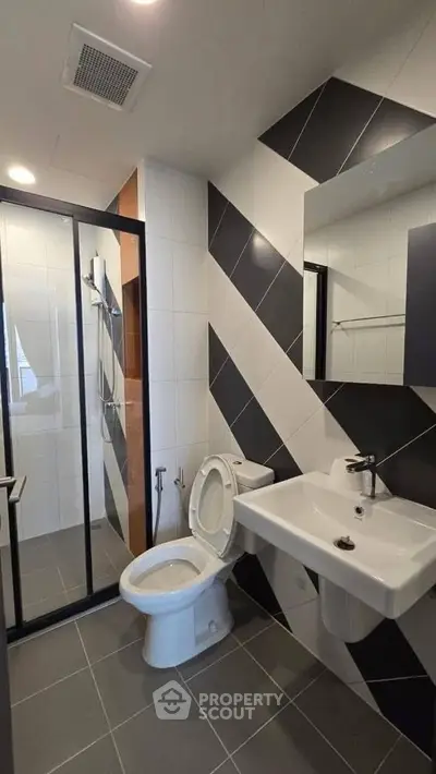 Modern bathroom with sleek black and white tiles and glass shower enclosure.