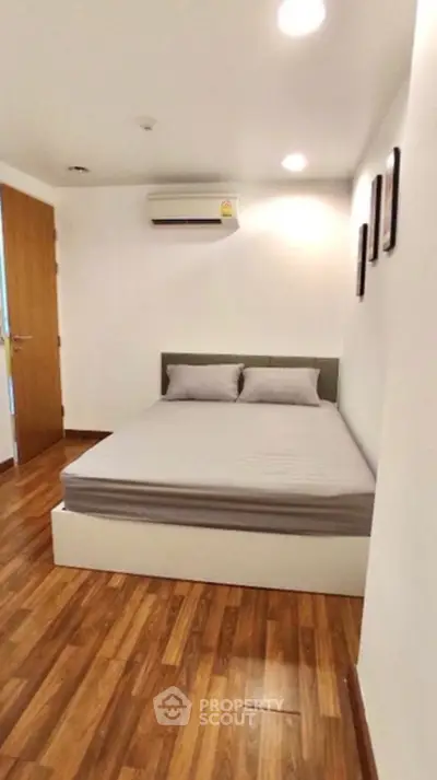 Cozy minimalist bedroom with wooden flooring and modern air conditioning.