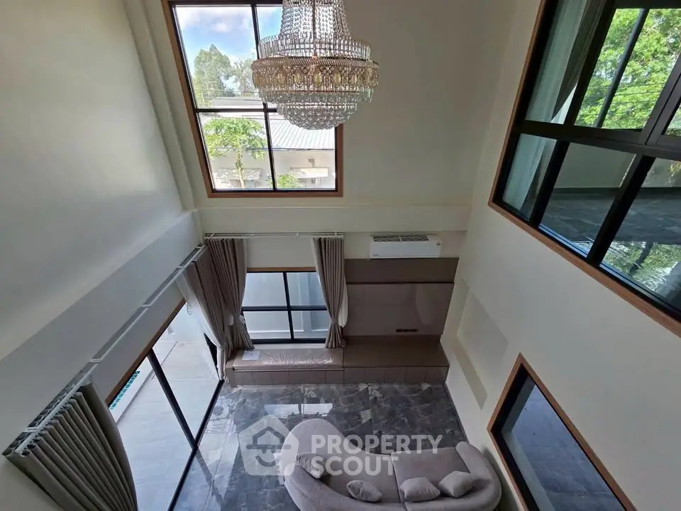 Luxurious high-ceiling living room with elegant chandelier and large windows offering natural light.