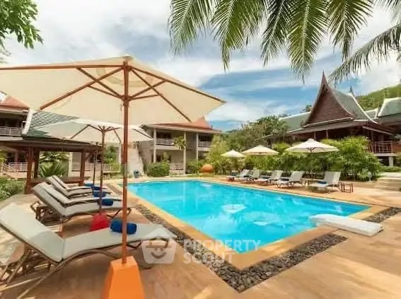 Luxurious tropical resort with inviting pool and sun loungers under palm trees.