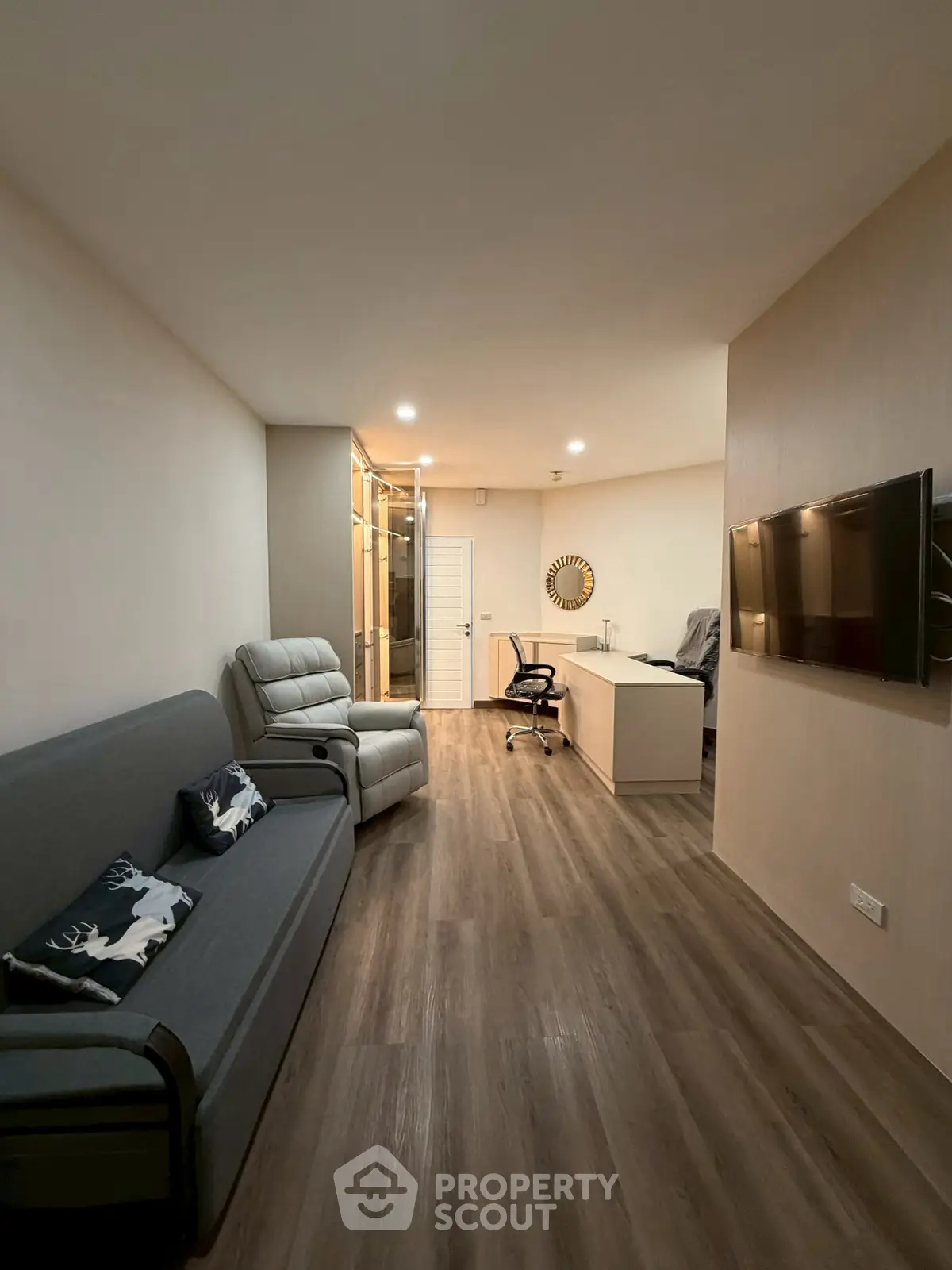 Modern living room with sleek furniture and wood flooring, featuring a wall-mounted TV and a cozy workspace.