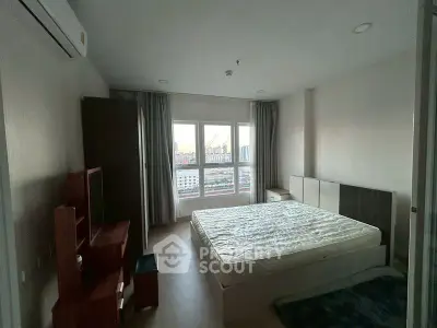 Spacious bedroom with large window offering city views, featuring modern furniture and ample natural light.