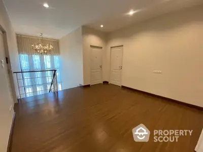 Spacious and elegant living room with gleaming hardwood floors, modern chandelier, and balcony access, perfect for upscale urban living.