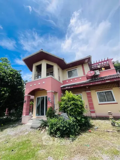 Charming two-story house with lush garden and spacious balcony under a clear blue sky.