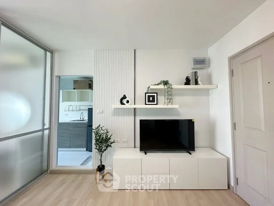Modern living room with sleek white furniture and minimalist decor, featuring a flat-screen TV and open shelving.