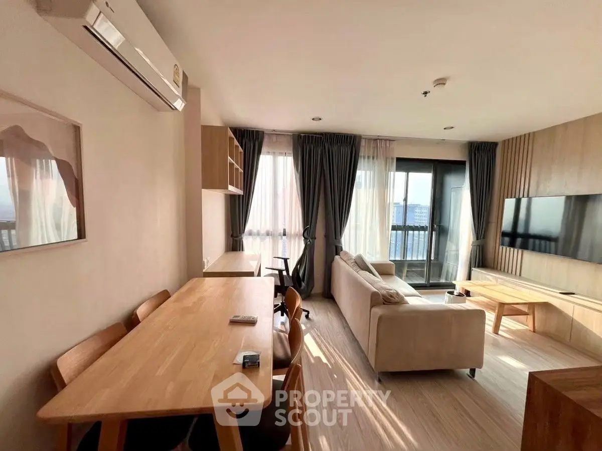 Spacious modern living room with large windows and balcony access, featuring stylish furniture and natural light.