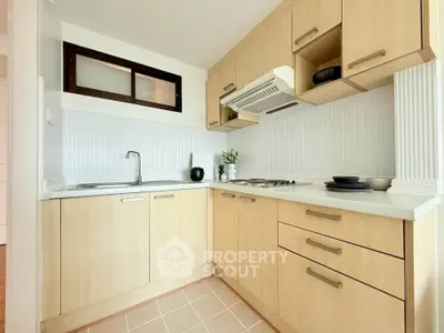 Modern kitchen with light wood cabinets and sleek appliances in a cozy apartment.