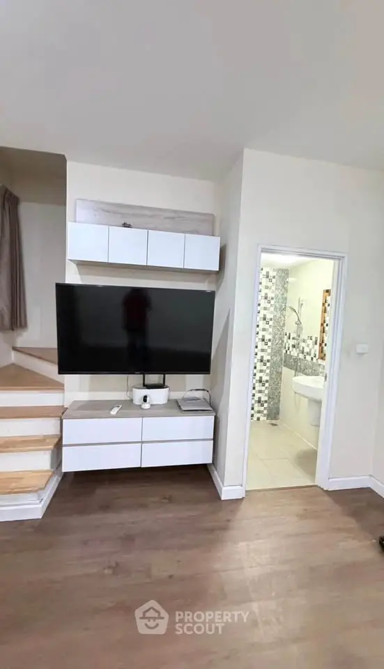Modern living room with sleek TV setup and staircase, adjacent to a stylish bathroom.
