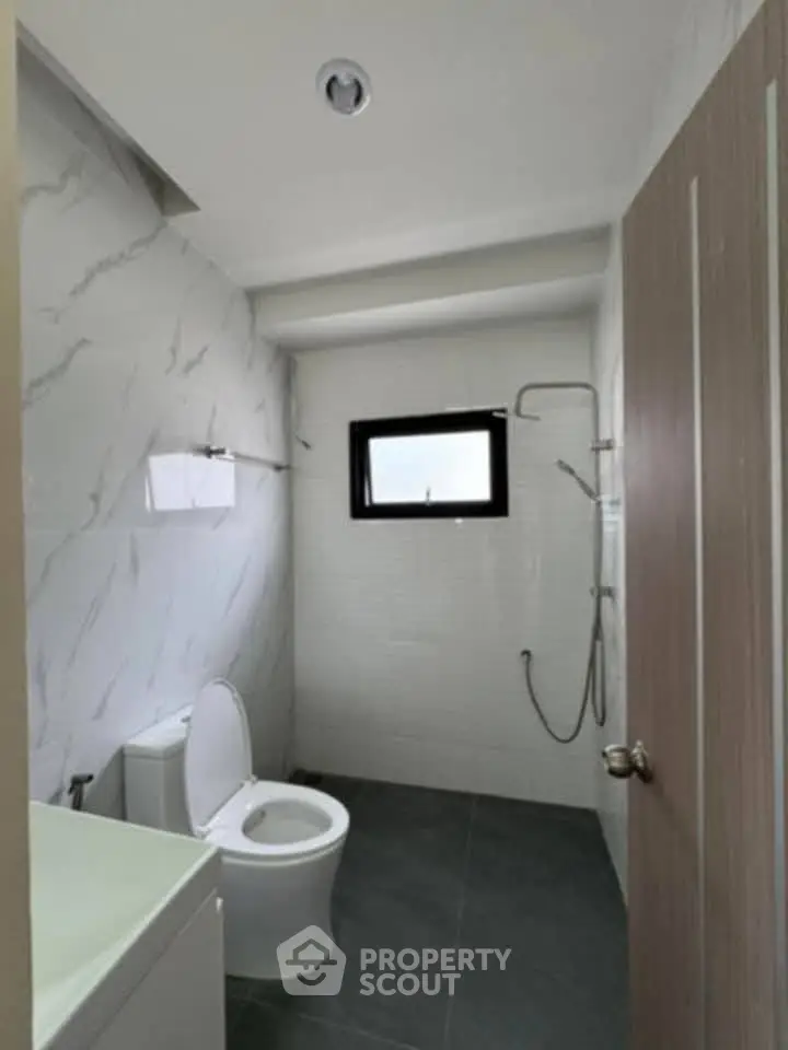 Modern bathroom with sleek design and marble walls, featuring a shower and toilet.