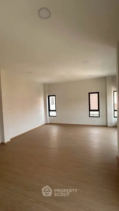 Spacious empty living room with wooden flooring and large windows for natural light.