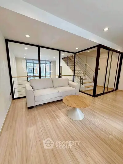Modern living room with glass walls and staircase, featuring a cozy sofa and stylish coffee table.