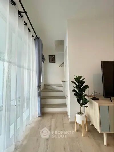 Modern living room with stylish decor and staircase, featuring light wood flooring and natural light.