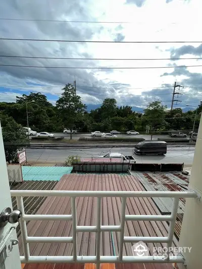 Charming balcony view overlooking a busy street with lush greenery and distant mountains.