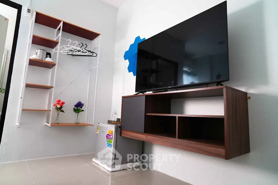 Modern living room with wall-mounted TV, sleek shelves, and compact fridge in a stylish apartment.