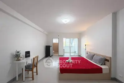 Spacious bedroom with modern decor and red bedding in a minimalist apartment.