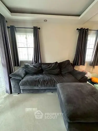 Spacious living room with plush dark sofa and natural light from large windows.