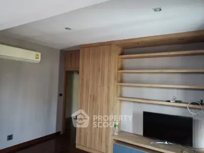 Spacious living room with built-in wooden shelves and modern air conditioning unit.
