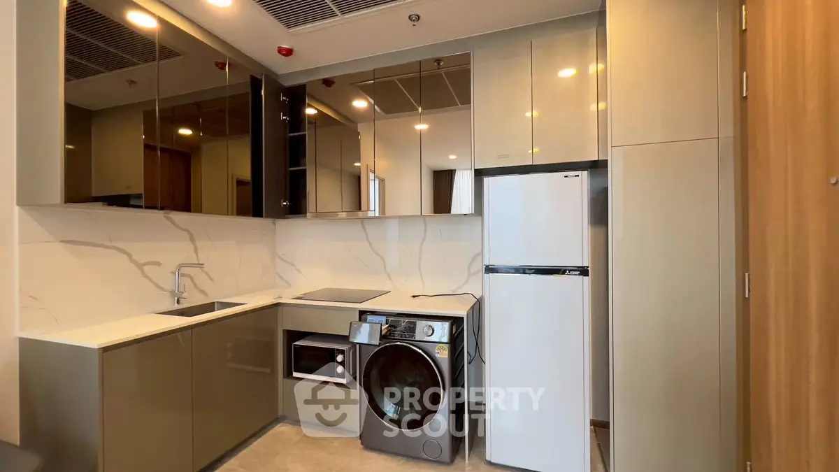 Modern kitchen with sleek cabinets, washing machine, and fridge in compact layout.