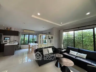 Spacious modern living room with open kitchen and large windows overlooking greenery.